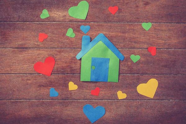 Ein buntes Haus aus Papier und bunte Herzen aus Papier liegen auf einem Holztisch | Valentinstag Immobilien Makler