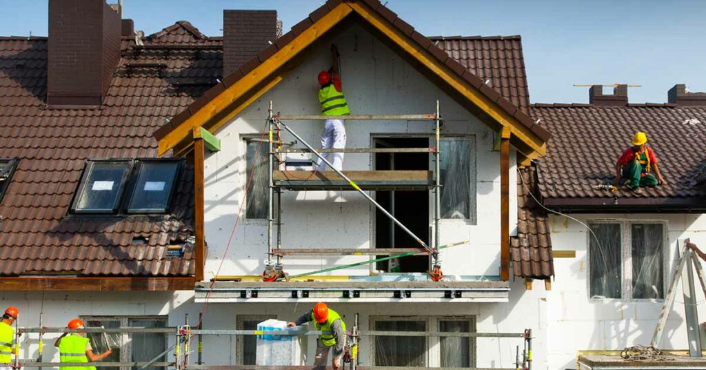 Mehrere Handwerker stehen auf einem Gerüst an einem Haus und arbeiten | Immobilie modernisieren sanieren